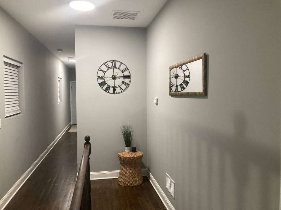 Inviting upstairs hallway with decorative wall clocks, wicker accent table and hardwood floors