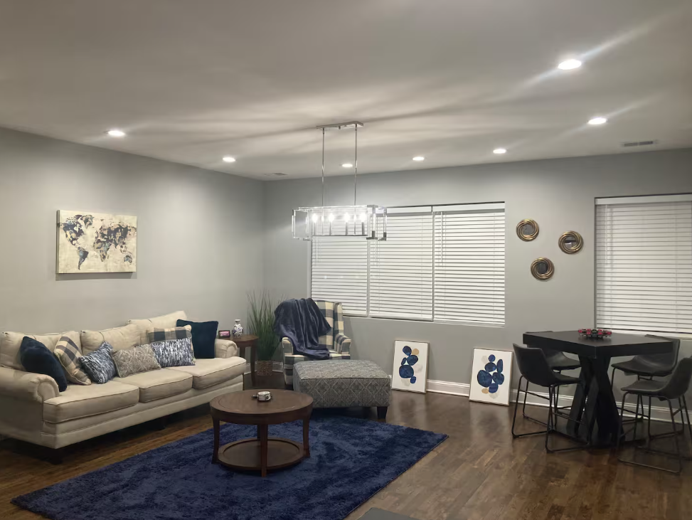 Furnished living and dining area with cream sofa, navy accents, modern chandelier, and wood flooring